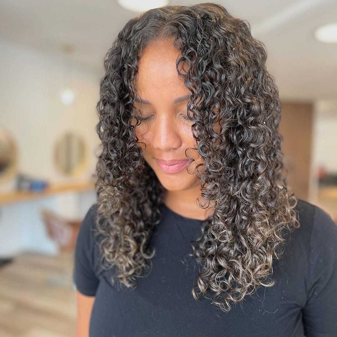 Woman with curly hair and a black shirt smiling softly in a modern, bright room.