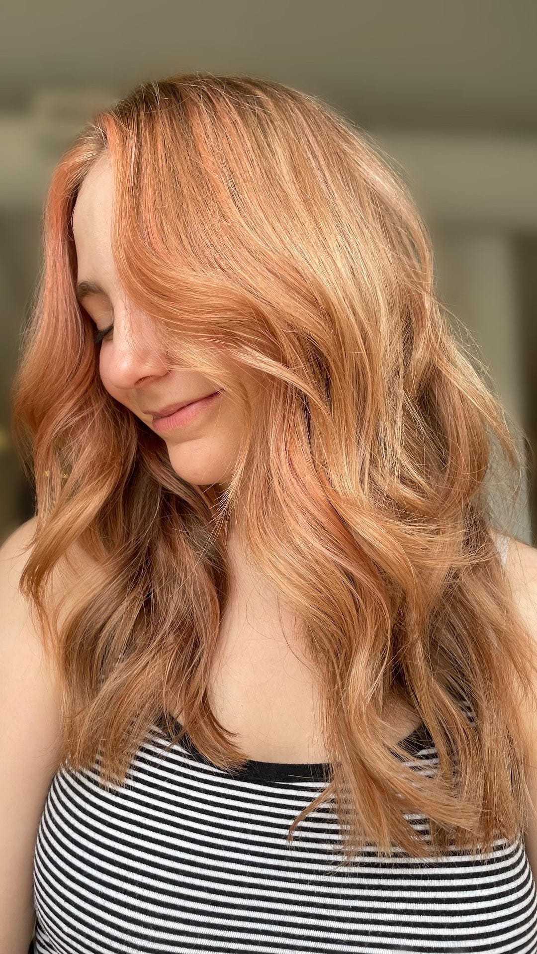 Woman with long, wavy, strawberry blonde hair looks down, wearing a striped tank top.