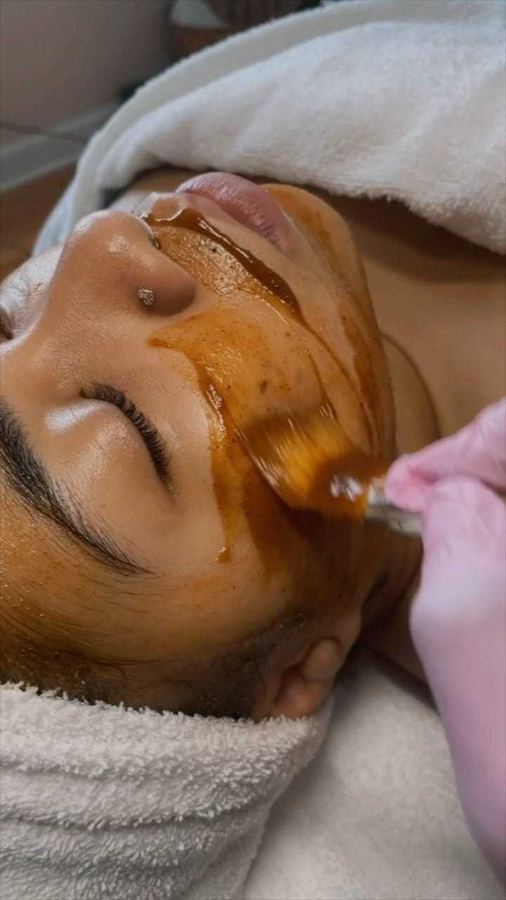 Person receiving a relaxing facial treatment with a brush applying a honey-like mask.
